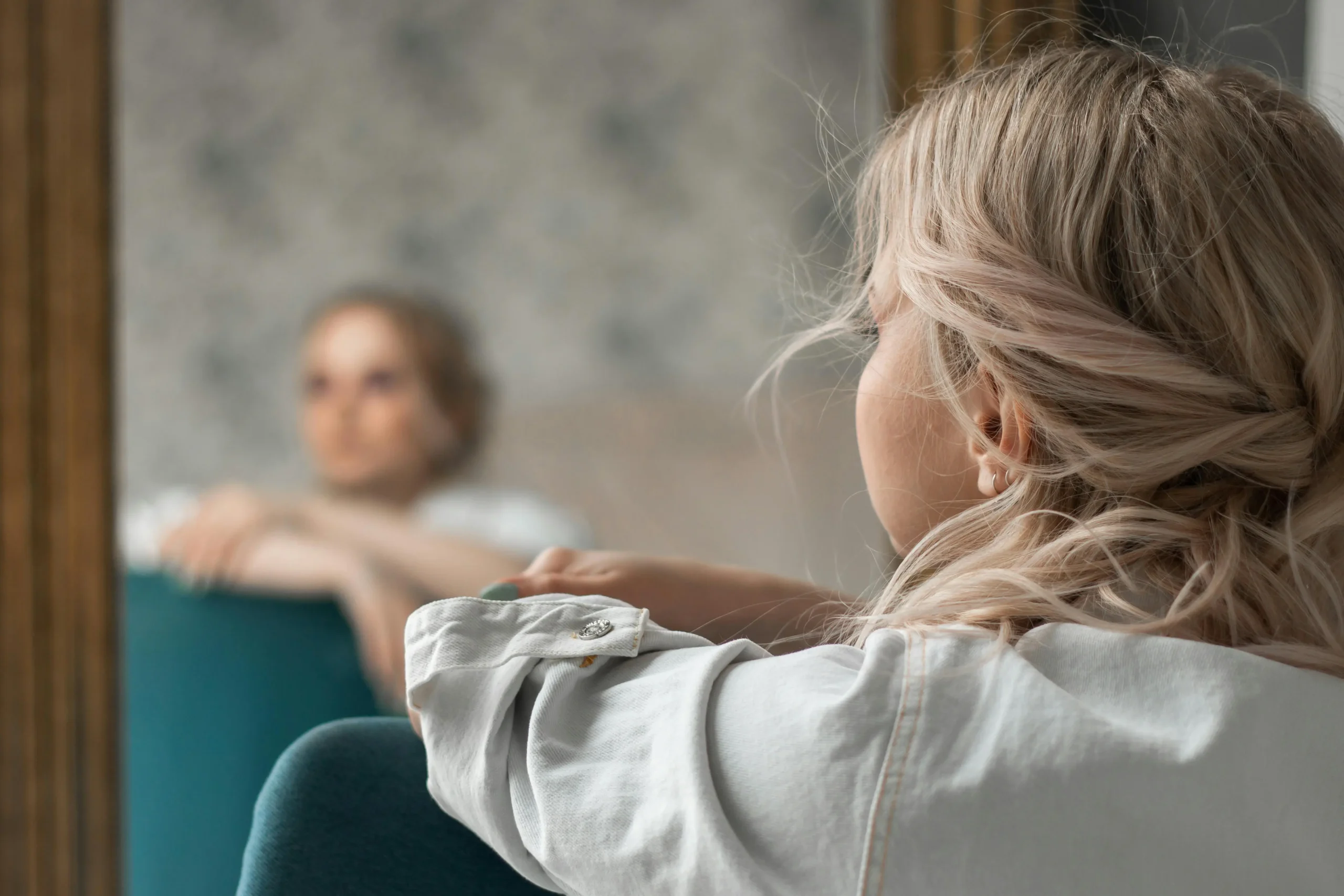 Affordable Counselling Network - Online Therapy UK - Woman seen from behind sitting in front of a mirror looking out the window