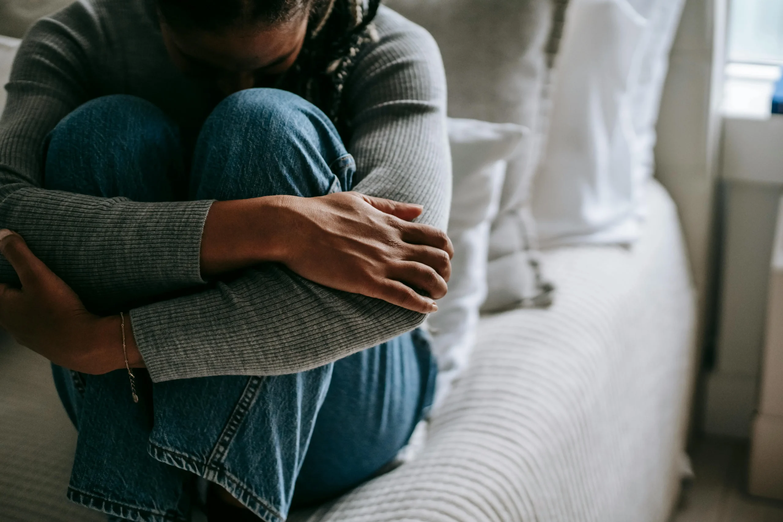 Affordable Counselling Network - Online Therapy UK - Person sitting on their bed holding their knees